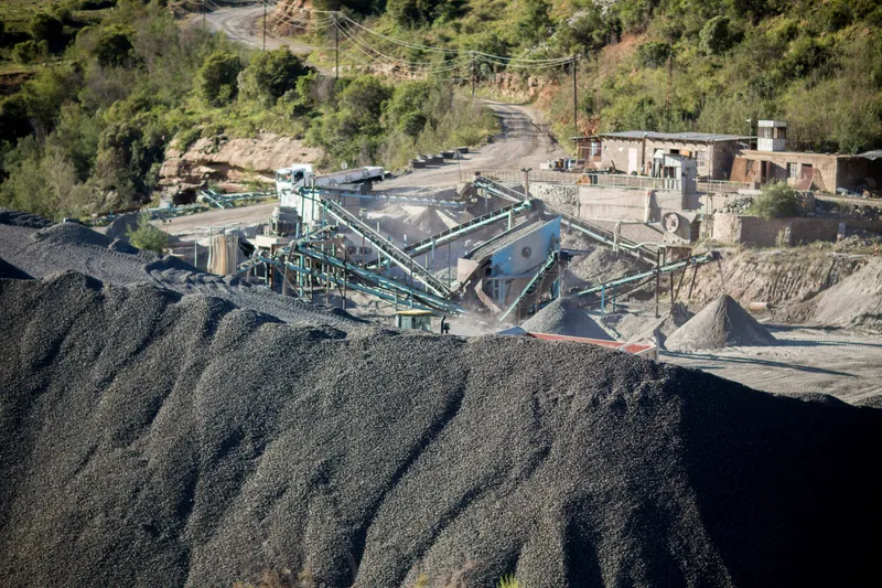 A crushing and screening plant with conveyors beside a large pile of dark crushed stone