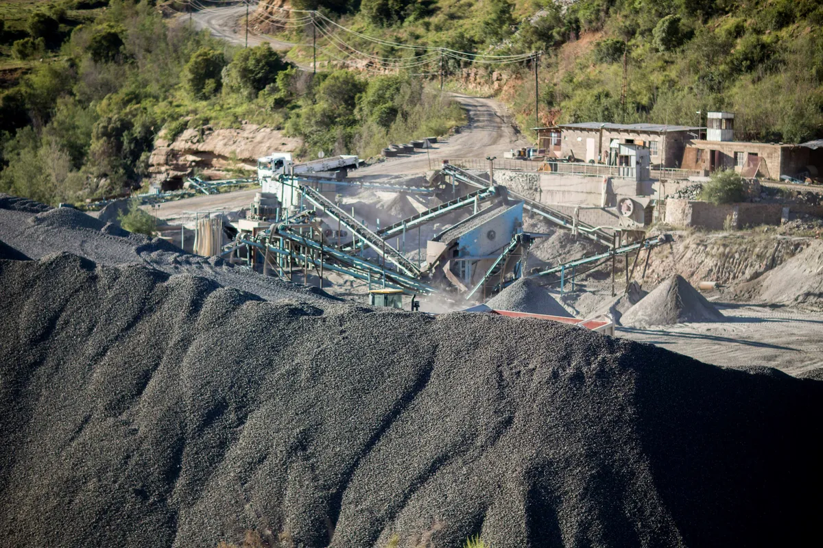 A crushing and screening plant with conveyors beside a large pile of dark crushed stone