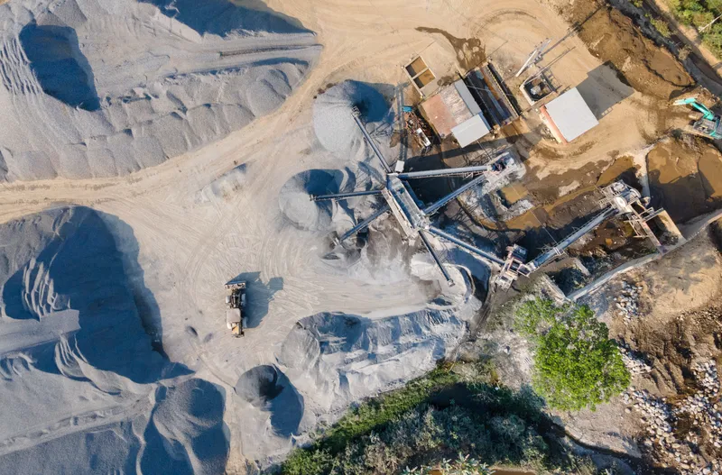 An aerial view of a rock crushing and stockpiling site with conveyors and a wheel loader