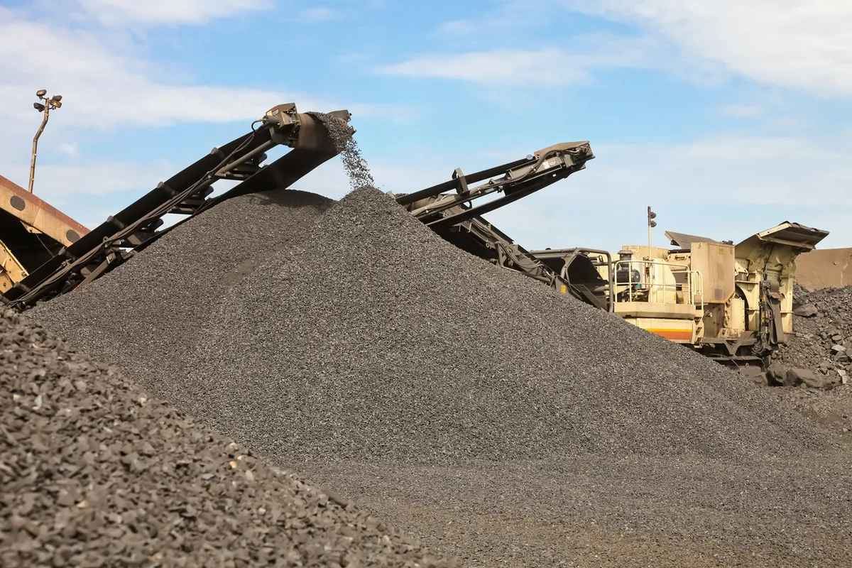 A conveyor dropping crushed stone onto a stockpile under a blue sky