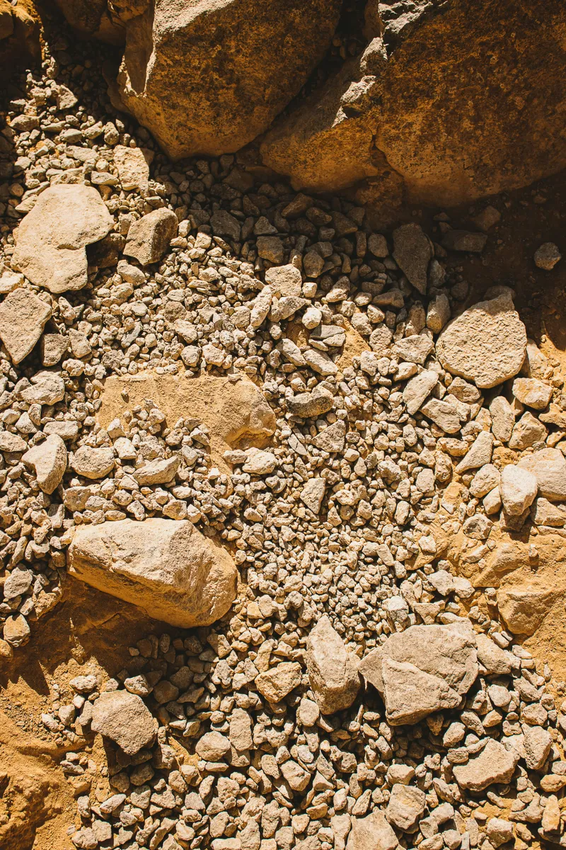 Loose yellow-brown gravel and larger rocks in strong sunlight